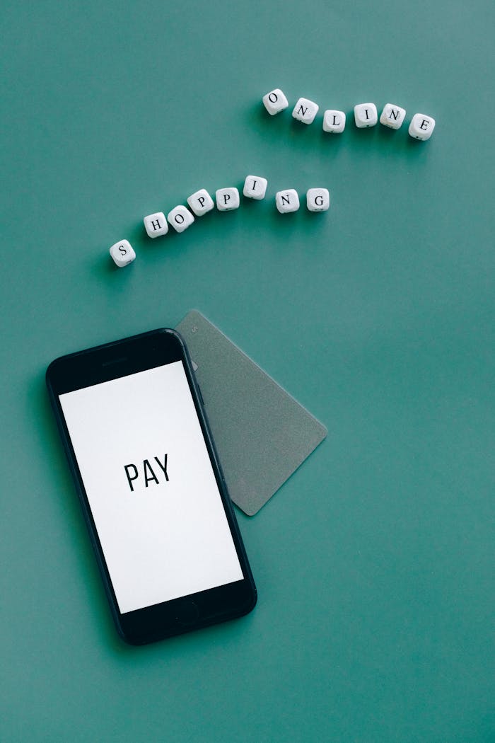 Smartphone with the word 'Pay' displayed alongside a card and letters spelling 'Shopping Online' on a green background.