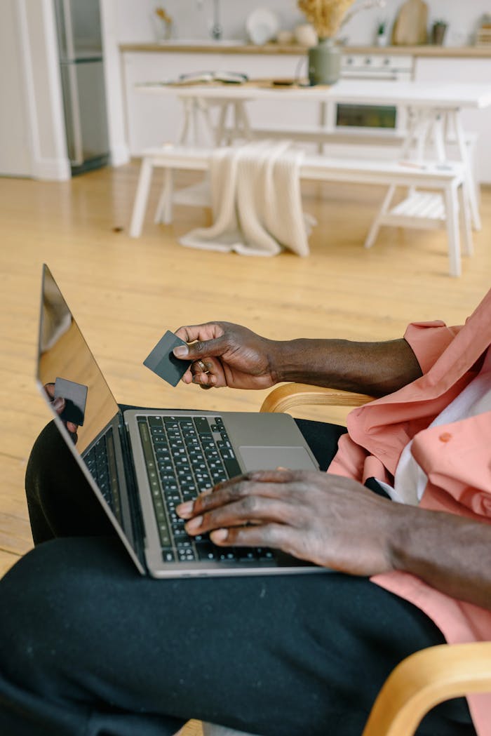 A person holding a credit card while using a laptop for online shopping in a cozy indoor setting.